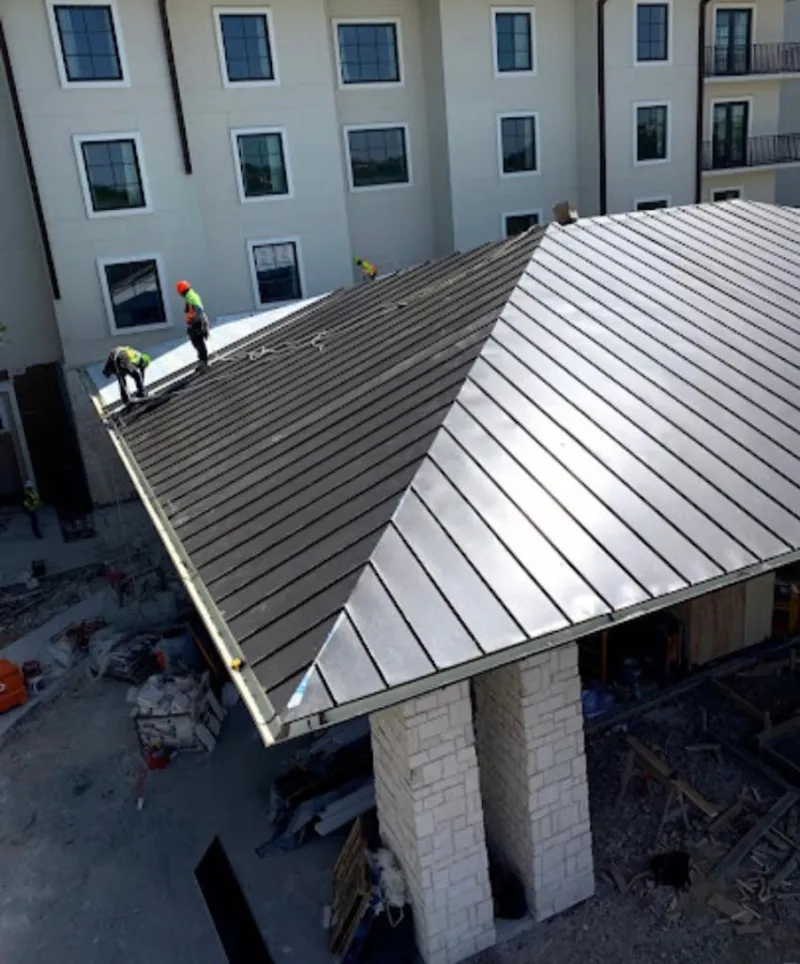 Crew installing standing seam metal roof panels on a commercial project in Parsons